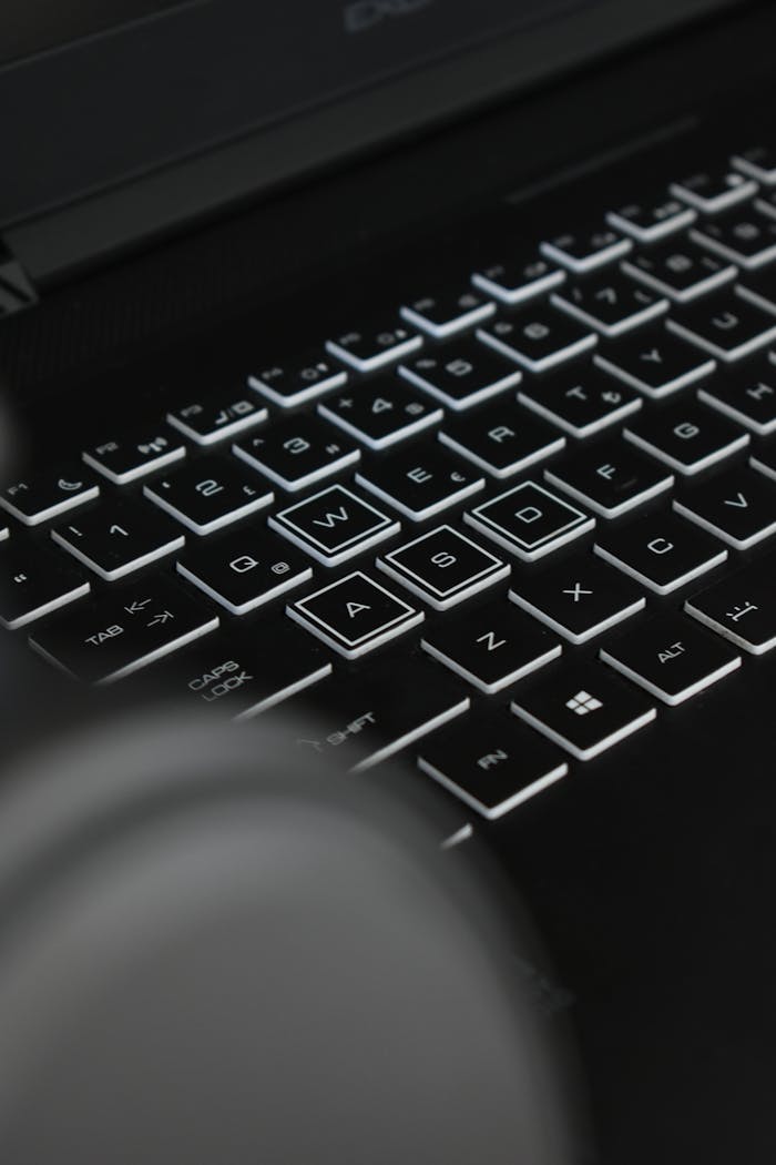 Close-up of black keyboard with glowing keys and letters, in low light.